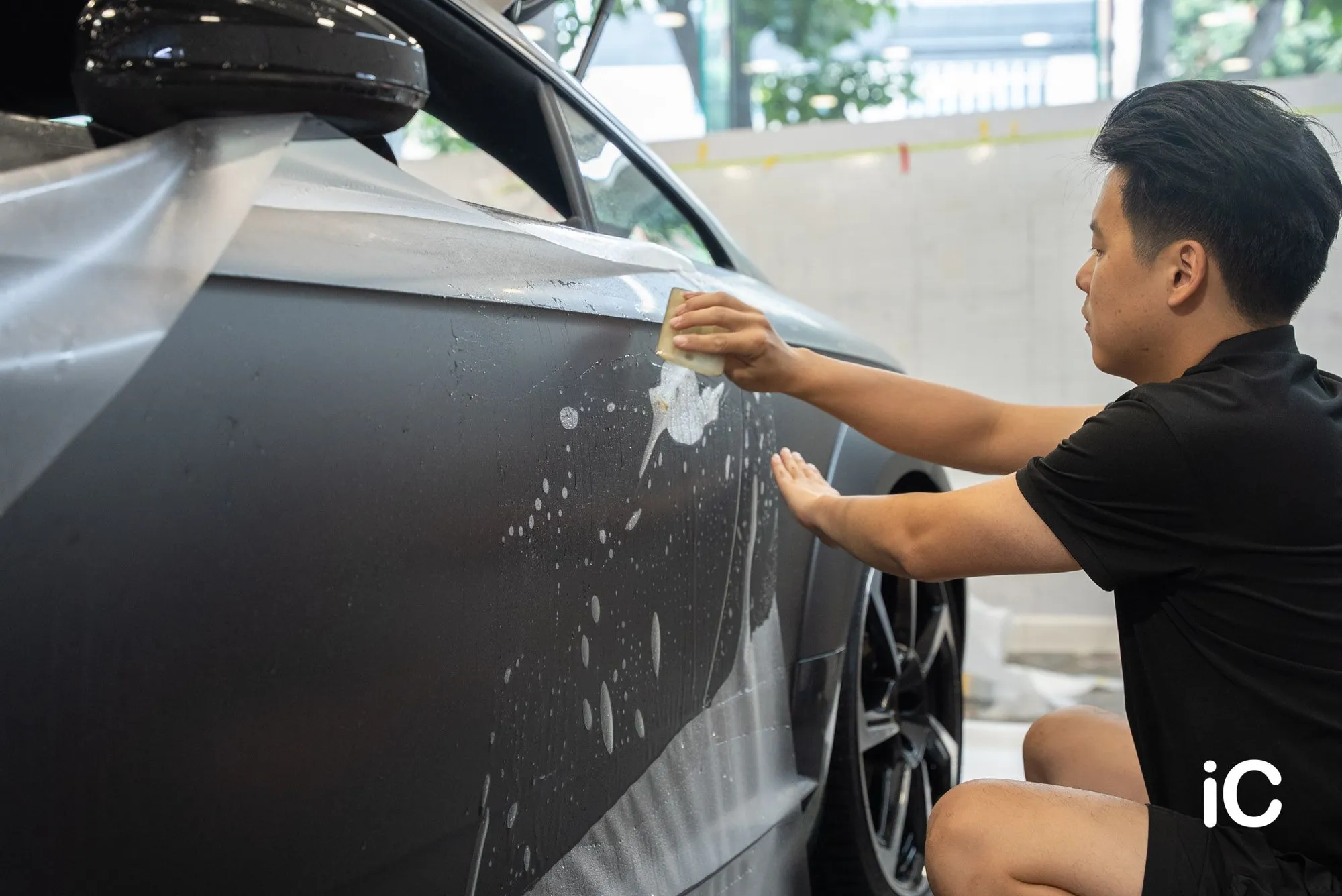 施工人員以刮板處理車門上的 PPF，車門表面可見貼膜用水